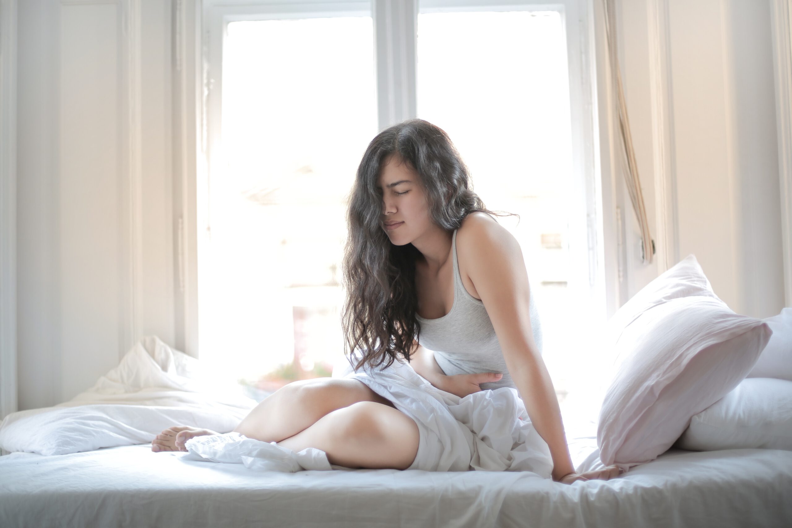 Kobieta w piżamach siedząca na łóżku z bólem brzucha